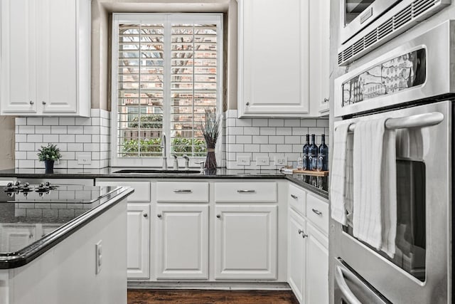 kitchen featuring dark countertops, backsplash, white cabinetry, stainless steel oven, and a sink