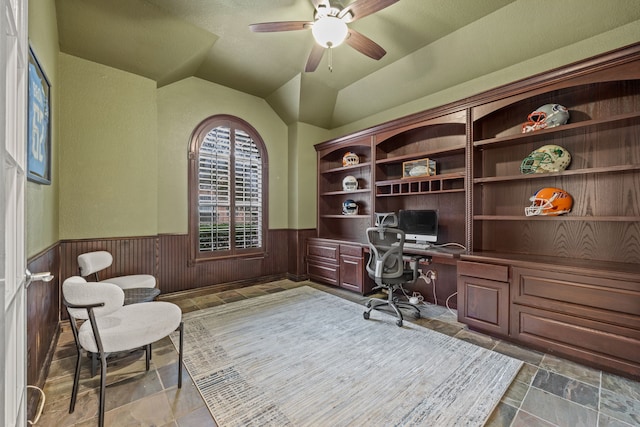 home office with ceiling fan, wooden walls, a wainscoted wall, vaulted ceiling, and built in study area