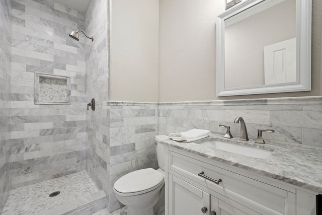 bathroom featuring toilet, a wainscoted wall, vanity, tile walls, and tiled shower