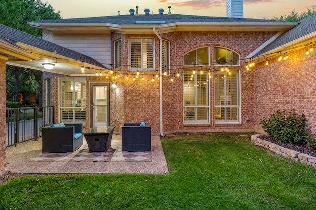 back of property at dusk with a chimney, fence, brick siding, a patio area, and a yard