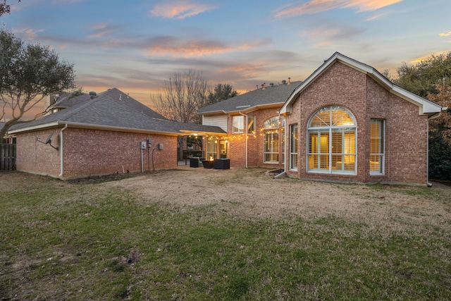 back of property featuring a yard, brick siding, and a shingled roof