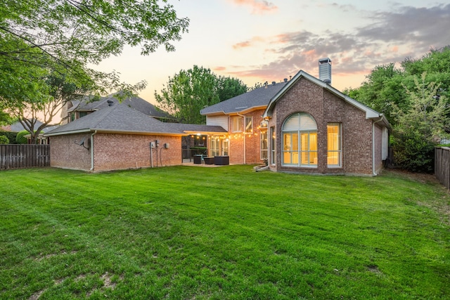 back of house at dusk featuring a yard, a sunroom, and a fenced backyard