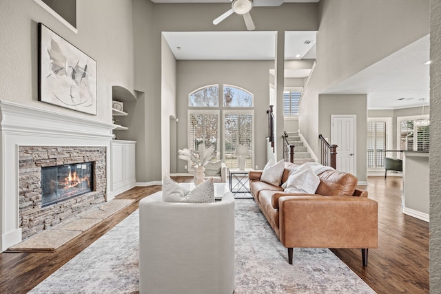 living area featuring built in features, a fireplace, a towering ceiling, light wood-style flooring, and baseboards