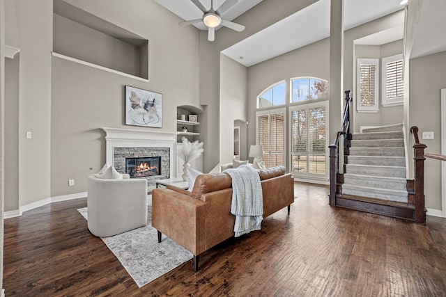 living room featuring built in shelves, stairs, a fireplace, and dark wood-style flooring