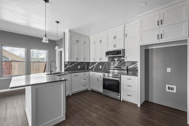 kitchen featuring a peninsula, a sink, appliances with stainless steel finishes, dark countertops, and decorative light fixtures