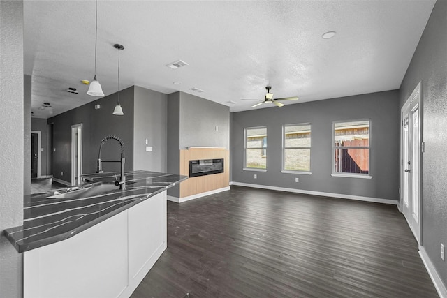 kitchen featuring dark wood-style flooring, hanging light fixtures, a glass covered fireplace, open floor plan, and white cabinetry