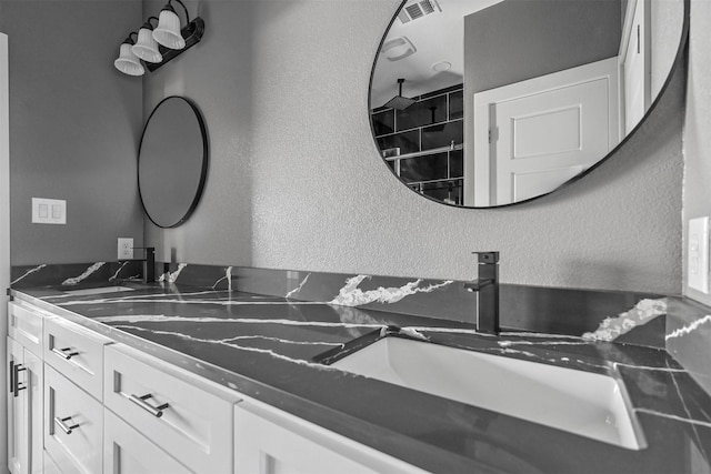 bathroom featuring visible vents, a textured wall, and vanity