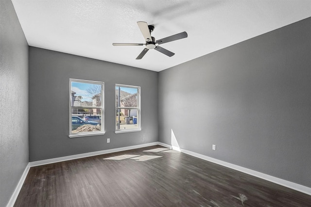 empty room featuring a textured wall, dark wood-type flooring, a ceiling fan, a textured ceiling, and baseboards