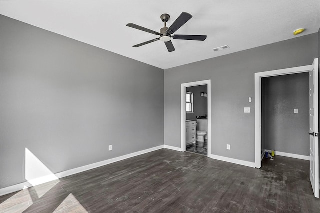 unfurnished bedroom featuring baseboards, visible vents, ensuite bath, ceiling fan, and dark wood-style flooring