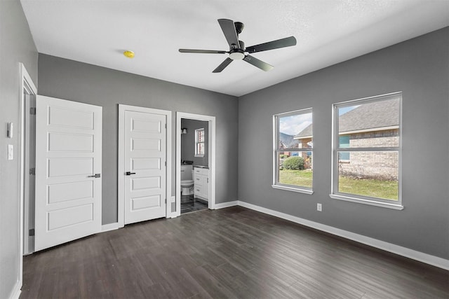 unfurnished bedroom featuring dark wood-type flooring, ceiling fan, ensuite bath, and baseboards