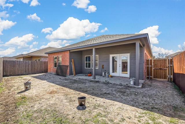 back of property with french doors, a fenced backyard, brick siding, and a gate