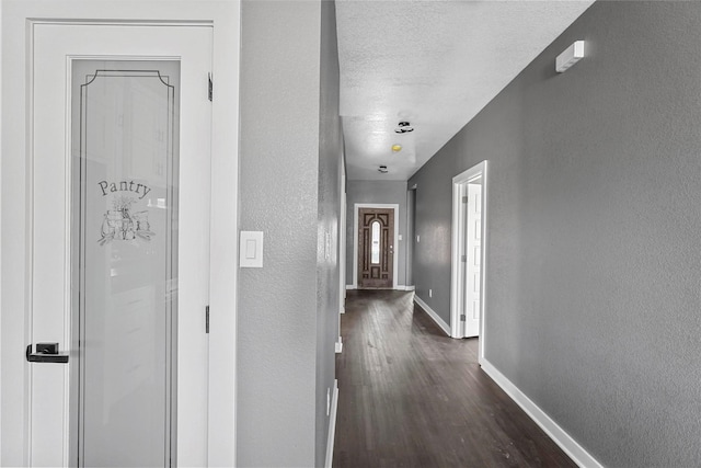 hall with a textured ceiling, baseboards, dark wood-type flooring, and a textured wall