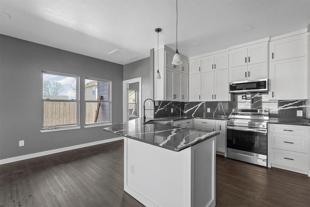 kitchen featuring hanging light fixtures, appliances with stainless steel finishes, white cabinets, a sink, and dark stone counters