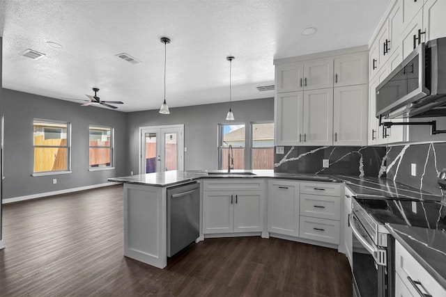 kitchen with appliances with stainless steel finishes, dark wood-type flooring, hanging light fixtures, white cabinetry, and a sink