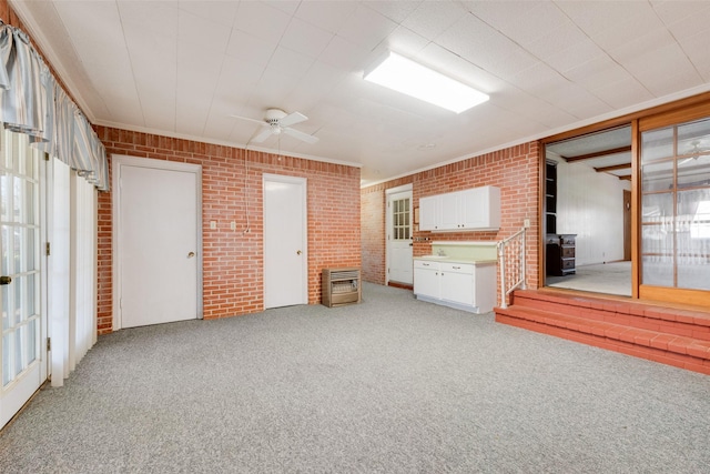 interior space with light carpet, brick wall, a ceiling fan, heating unit, and a wood stove