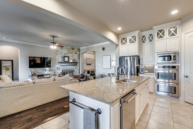 kitchen featuring a center island with sink, appliances with stainless steel finishes, glass insert cabinets, white cabinetry, and a sink