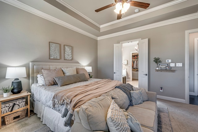 bedroom featuring light colored carpet, baseboards, ornamental molding, a tray ceiling, and a walk in closet