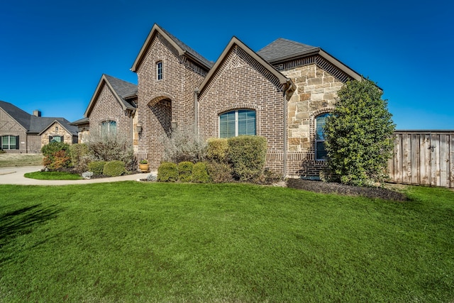 french country inspired facade with a front yard, stone siding, and brick siding