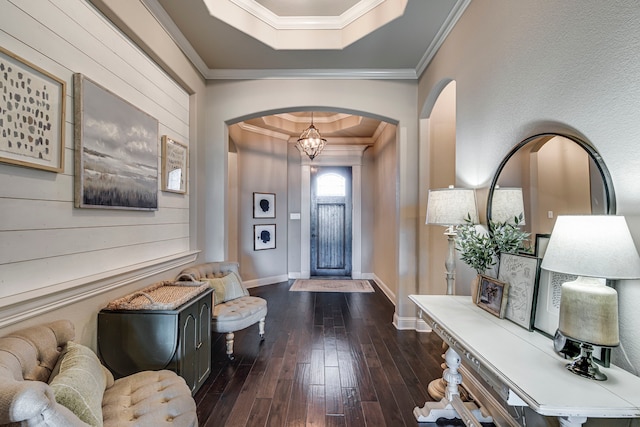 foyer entrance featuring dark wood-style floors, a tray ceiling, arched walkways, ornamental molding, and baseboards