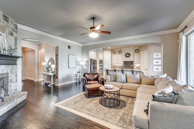 living area with dark wood-style floors, arched walkways, crown molding, and a stone fireplace