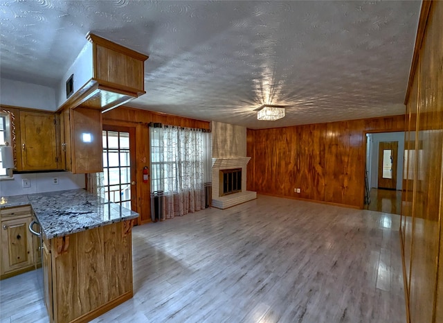 kitchen with light stone counters, a brick fireplace, wood walls, and light wood-style flooring