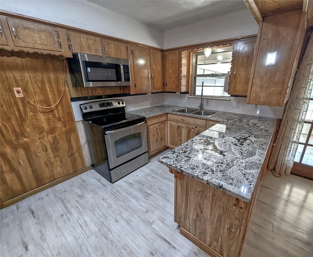 kitchen featuring light wood finished floors, appliances with stainless steel finishes, brown cabinets, and a sink