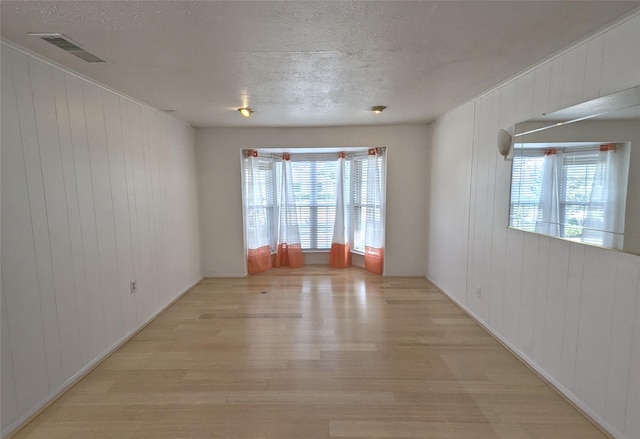 unfurnished room with a healthy amount of sunlight, visible vents, light wood-style flooring, and a textured ceiling