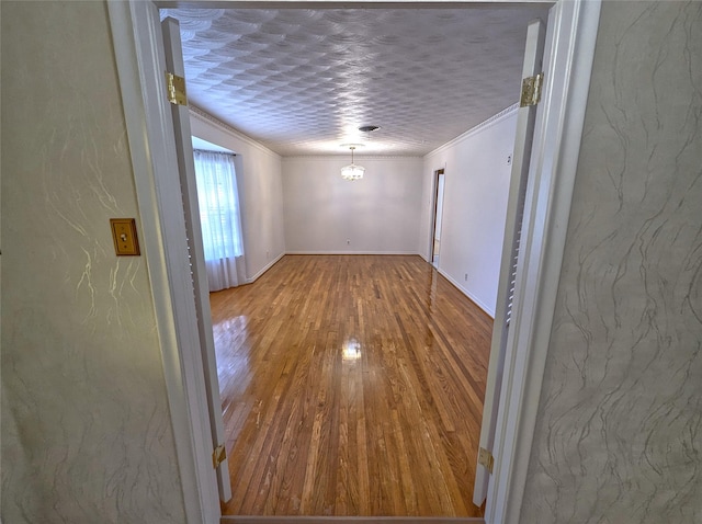 unfurnished room featuring a textured wall, wood finished floors, baseboards, ornamental molding, and an inviting chandelier