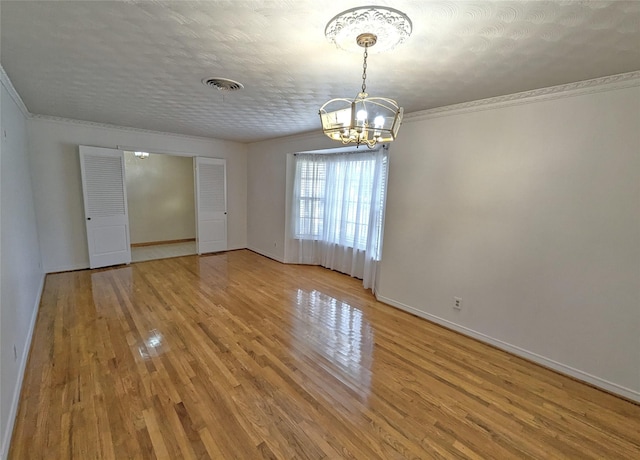 unfurnished room featuring a notable chandelier, wood finished floors, visible vents, baseboards, and crown molding