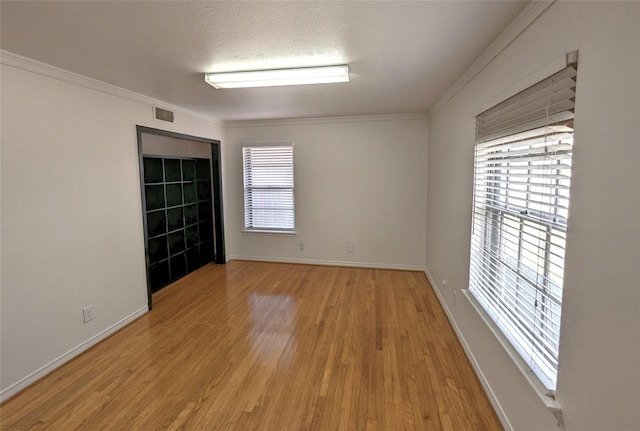 spare room featuring light wood-type flooring, baseboards, ornamental molding, and a textured ceiling