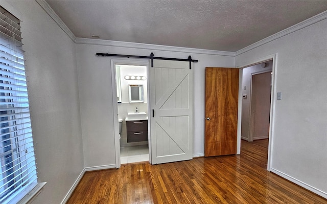 unfurnished bedroom with ornamental molding, dark wood-style flooring, a textured ceiling, and a barn door