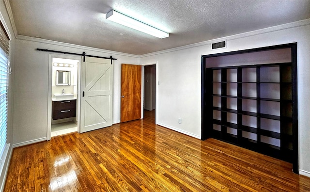 unfurnished bedroom featuring a barn door, visible vents, dark wood finished floors, crown molding, and a sink