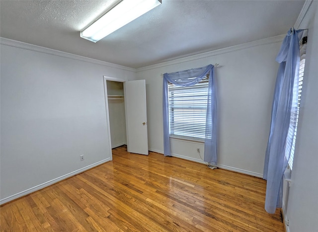 unfurnished bedroom featuring a textured ceiling, ornamental molding, wood finished floors, and baseboards