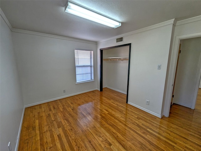 unfurnished bedroom with baseboards, visible vents, wood finished floors, crown molding, and a closet