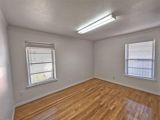 empty room with ornamental molding, wood finished floors, and baseboards