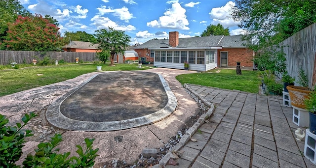 back of house featuring brick siding, a patio area, a fenced backyard, and a sunroom