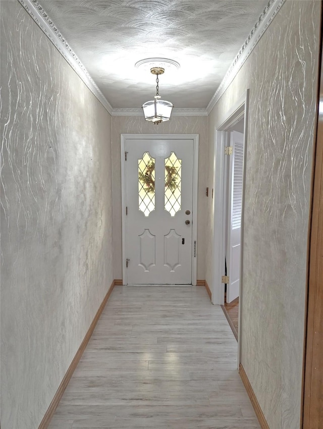 doorway with baseboards, a textured wall, light wood-style floors, and crown molding