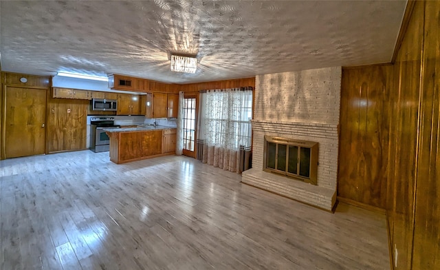 kitchen with brown cabinets, light wood finished floors, light countertops, appliances with stainless steel finishes, and open floor plan