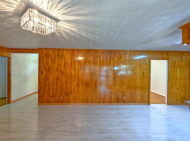 spare room featuring baseboards, wooden walls, and light wood finished floors