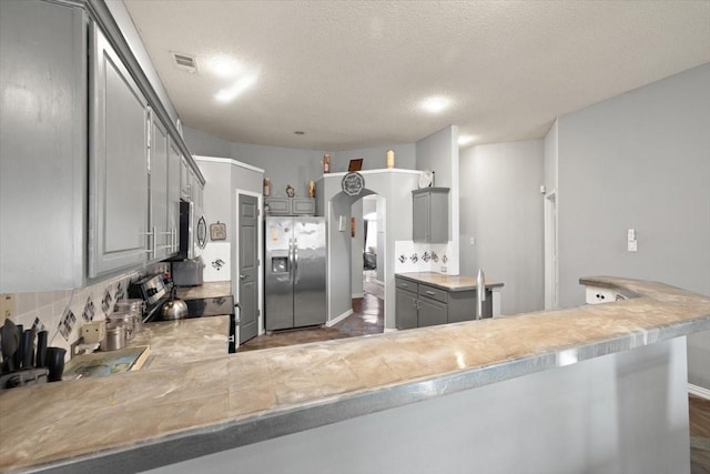 kitchen with a peninsula, gray cabinets, stainless steel appliances, and light countertops