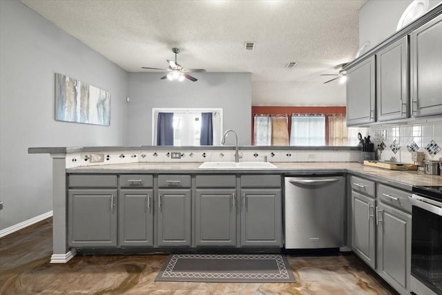 kitchen featuring appliances with stainless steel finishes, gray cabinets, a sink, and a peninsula