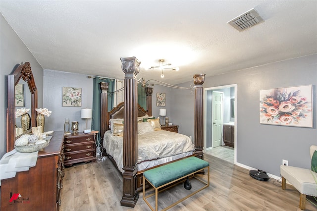 bedroom with light wood finished floors, baseboards, visible vents, ensuite bath, and a textured ceiling