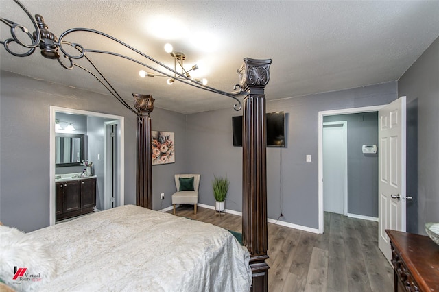 bedroom featuring a textured ceiling, ensuite bathroom, wood finished floors, baseboards, and ornate columns