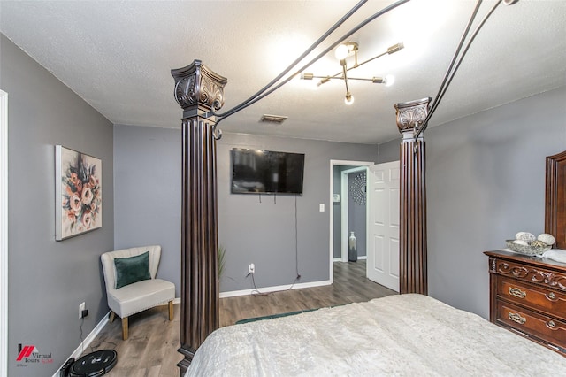 bedroom featuring decorative columns, baseboards, visible vents, wood finished floors, and a textured ceiling