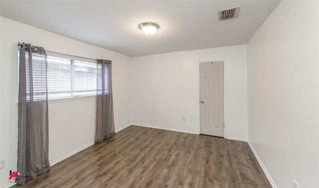 unfurnished room featuring dark wood-style flooring, visible vents, and baseboards