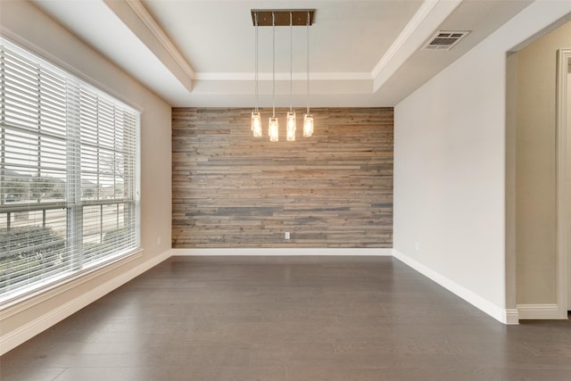 unfurnished dining area with wooden walls, an accent wall, dark wood-type flooring, visible vents, and a raised ceiling