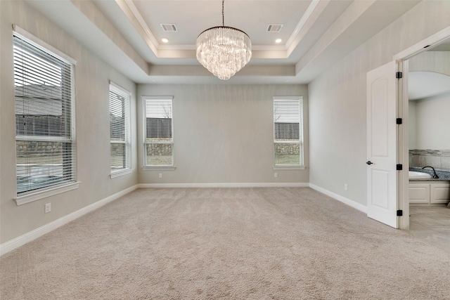 spare room featuring light carpet, an inviting chandelier, visible vents, and a raised ceiling