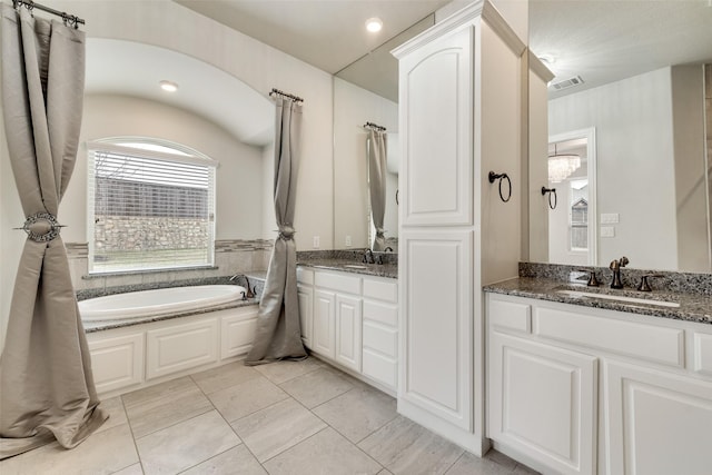 bathroom featuring a garden tub, visible vents, two vanities, and a sink