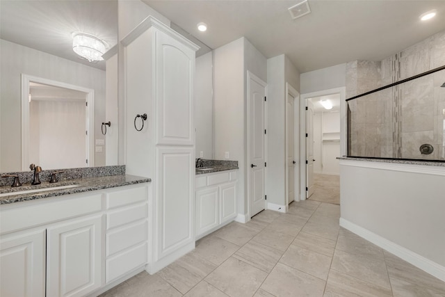 bathroom with a stall shower, baseboards, visible vents, a sink, and two vanities