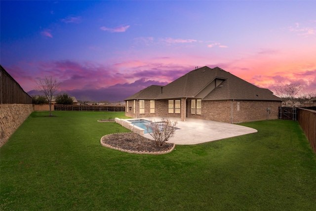 back of property at dusk featuring a lawn, a patio, a fenced backyard, roof with shingles, and brick siding